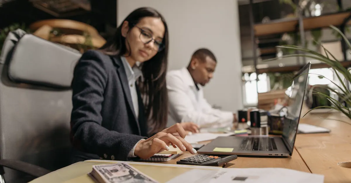 Two accounting professionals reviewing documents and comparing software options on a laptop