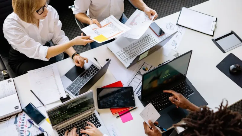 Team collaborating on documents using laptops and tablets in a modern workspace